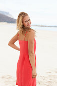 A young blonde woman on a beach wearing a red summer dress