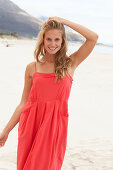 Junge blonde Frau in rotem Sommerkleid am Strand