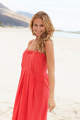 A young blonde woman on a beach wearing a red summer dress