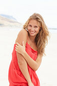 A young blonde woman on a beach wearing a red summer dress