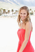 A young blonde woman on a beach wearing a red summer dress