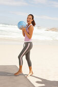 A young brunette woman by the sea wearing sports clothes with a ball