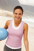 Junge brünette Frau in sportlicher Kleidung mit Ball am Meer