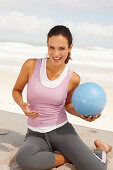 A young brunette woman by the sea wearing sports clothes with a ball