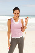 A young brunette woman by the sea wearing sports clothes with a skipping rope