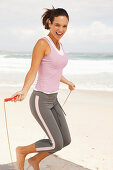 A young brunette woman by the sea wearing sports clothes with a skipping rope