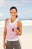 A young brunette woman by the sea wearing sports clothes with a dumbbell