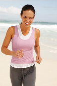 Junge brünette Frau in sportlicher Kleidung joggt am Meer