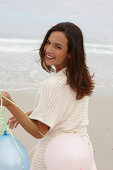 A brunette woman wearing a short-sleeved cardigan and holding balloons