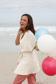 A brunette woman wearing a short-sleeved cardigan and holding balloons