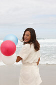 A brunette woman wearing a short-sleeved cardigan and holding balloons