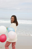 A brunette woman wearing a short-sleeved cardigan and holding balloons