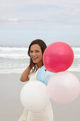 A brunette woman wearing a short-sleeved cardigan and holding balloons