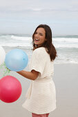 A brunette woman wearing a short-sleeved cardigan and holding balloons