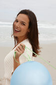 A brunette woman wearing a short-sleeved cardigan and holding a balloon