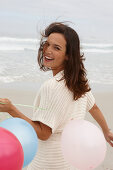 A brunette woman wearing a short-sleeved cardigan and holding a balloon