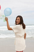 A brunette woman wearing a short-sleeved cardigan and holding balloons