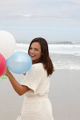 A brunette woman wearing a short-sleeved cardigan and holding a balloon