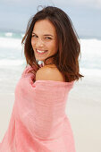 A brunette woman by the sea with a pink shawl