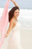 Brünette Frau in weißem Sommerkleid auf rosa Tuch liegend am Meer
