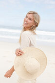 Blonde Frau mit Sommerhut in hellem Cardigan am Strand