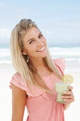 A young woman on a beach with a smoothie wearing a pink top