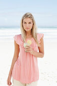 A young woman on a beach with a smoothie wearing a pink top