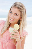 A young woman on a beach with a smoothie wearing a pink top