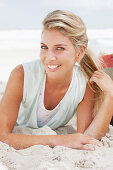 A blonde woman lying on the beach wearing a light t-shirt