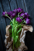 'Purple peony' tulips in brown paper on wooden surface