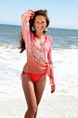 Brünette Frau in rosa Bluse mit Pailletten und Bikini am Strand
