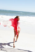 Brünette Frau mit Strandtuch in rosa Bluse und Bikini am Meer