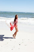 A brunette woman with a beach towel wearing a pink blouse and a bikini by the sea