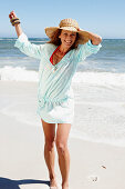 Brünette Frau mit Hut in hellblauem Strandkleid am Meer