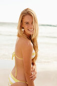 A blonde woman on a beach wearing a white and yellow bikini