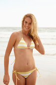 A blonde woman on a beach wearing a white and yellow bikini