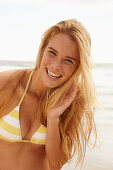 A blonde woman on a beach wearing a white and yellow bikini