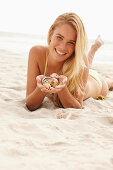 Blonde Frau mit Muschelschalen am Strand liegend