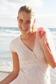 A blonde woman by the sea wearing a white embroidered dress