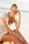 A blonde woman by the sea wearing a white embroidered dress