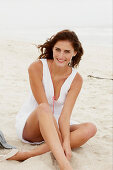 A brunette woman on a beach wearing a white summer dress