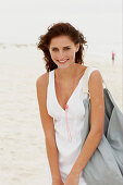 A brunette woman by the sea with a bag wearing a white summer dress