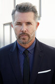 A man with a bread wearing a blue shirt with a tie and a blazer