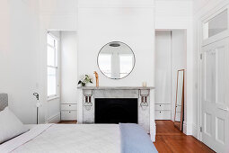Double bed, closed fireplace, round mirror above in white bedroom
