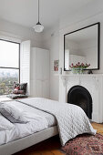 Double bed with quilt in front of fireplace in white bedroom