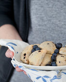 A woman holding a platter of blueberry scones with fresh blueberries