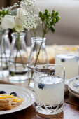 A brunch table with lemonade with blueberries, lemon tart and flowers