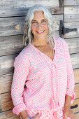 Reife Frau in rosa Bluse vor Holzwand
