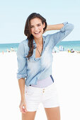 A young woman on a beach wearing a denim shirt and white shorts