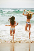 Zwei Frauen in Bikinis und mit Sommerhut am Strand